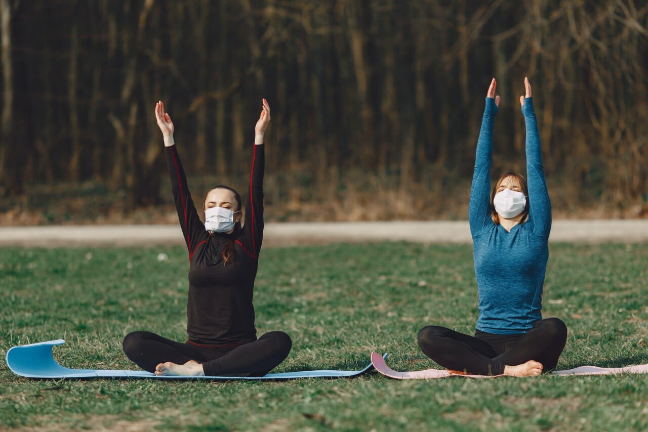 Two women practicing yoga outside during COVID-19 with masks