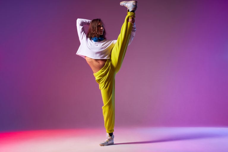 Active smile woman standing with back towards camera, doing split leap in the air, showing dancing skills, training in dance studio, artistic impression, indoor shot