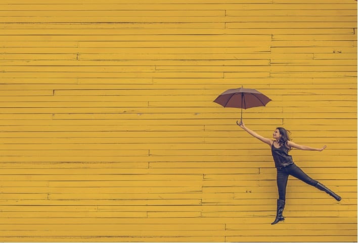 Creative artist jumping and holding umbrella in front of yellow backdrop