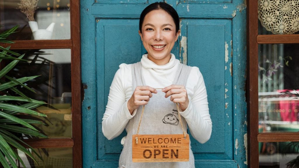 Small business owner holding Welcome We Are Open sign