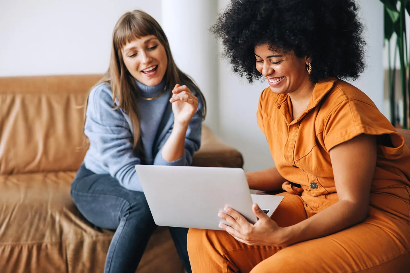 Two young women having a discussion while looking at a laptop screen in an office